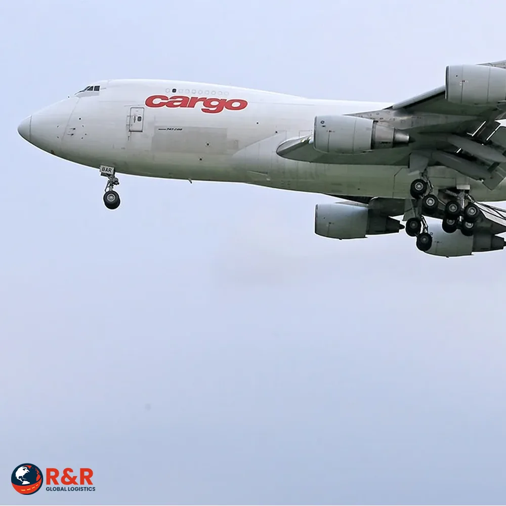A white cargo plane in flight with the R&R Global Logistics logo
